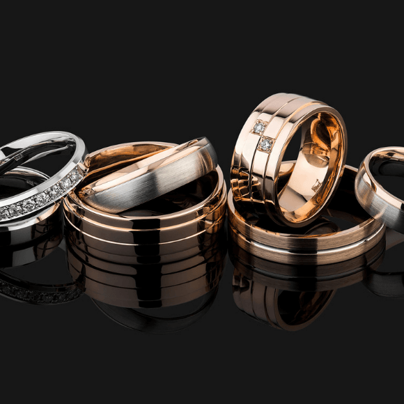 Auksiniai ir balto aukso žiedai su deimantų detalėmis ant juodo atspindinčio paviršiaus