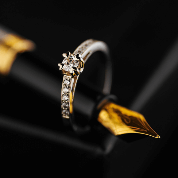 Auksinis žiedas su centriniu akmeniu ir smulkiais akmenėliais juostoje