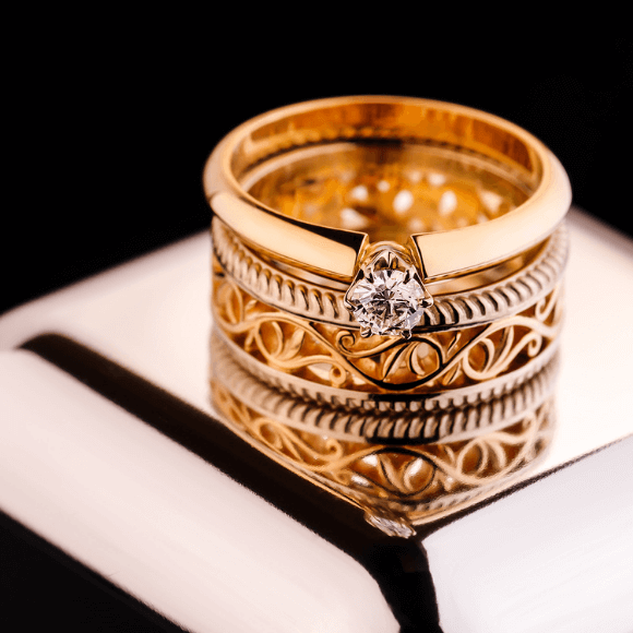 Auksinis žiedas su centriniu deimantu ant metalinio paviršiaus