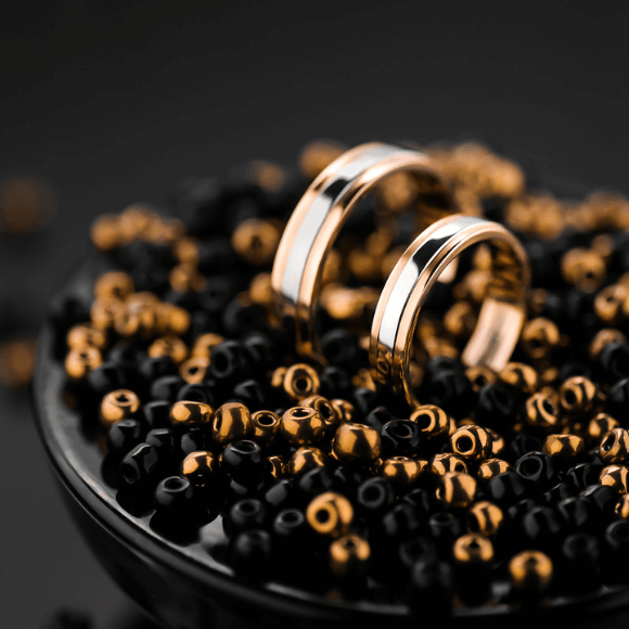 Du auksiniai žiedai padėti ant juodų ir auksinių karoliukų