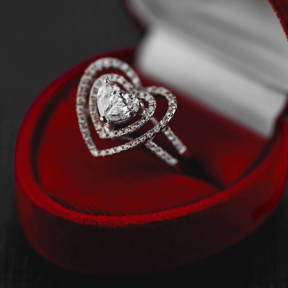 Širdelės formos žiedas su centriniu akmeniu ir smulkiais akmenėliais, padėtas raudonoje dėžutėje